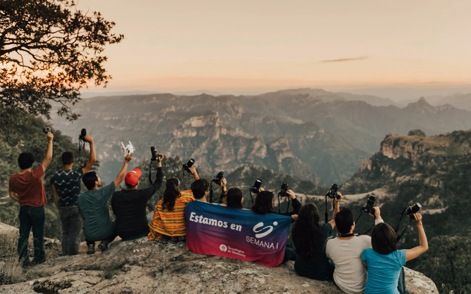 Jovenes sostienendo cámaras fotográficas sentados en un acantilado