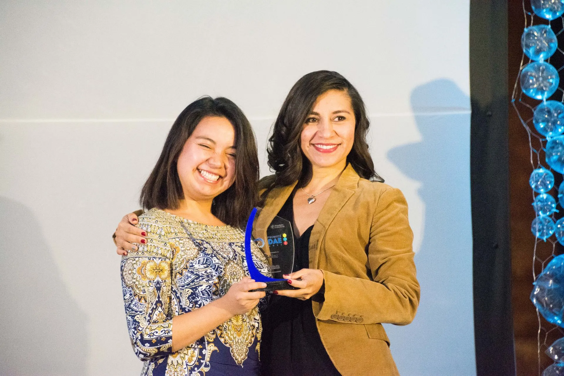 Maestra abrazando a su alumno sosteniendo un premio