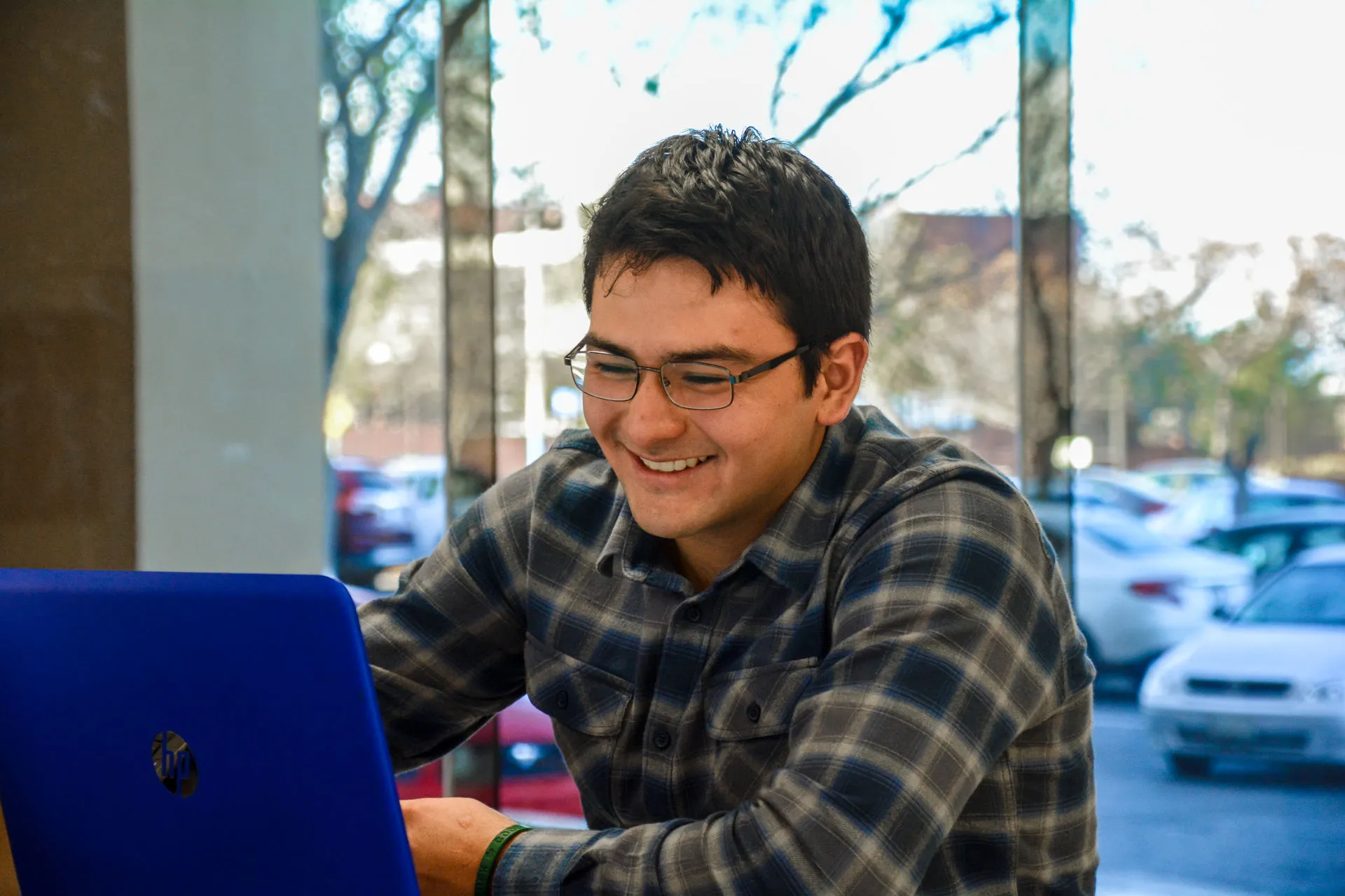 Joven sonriendo mientras observa la pantalla de su computadora portatil