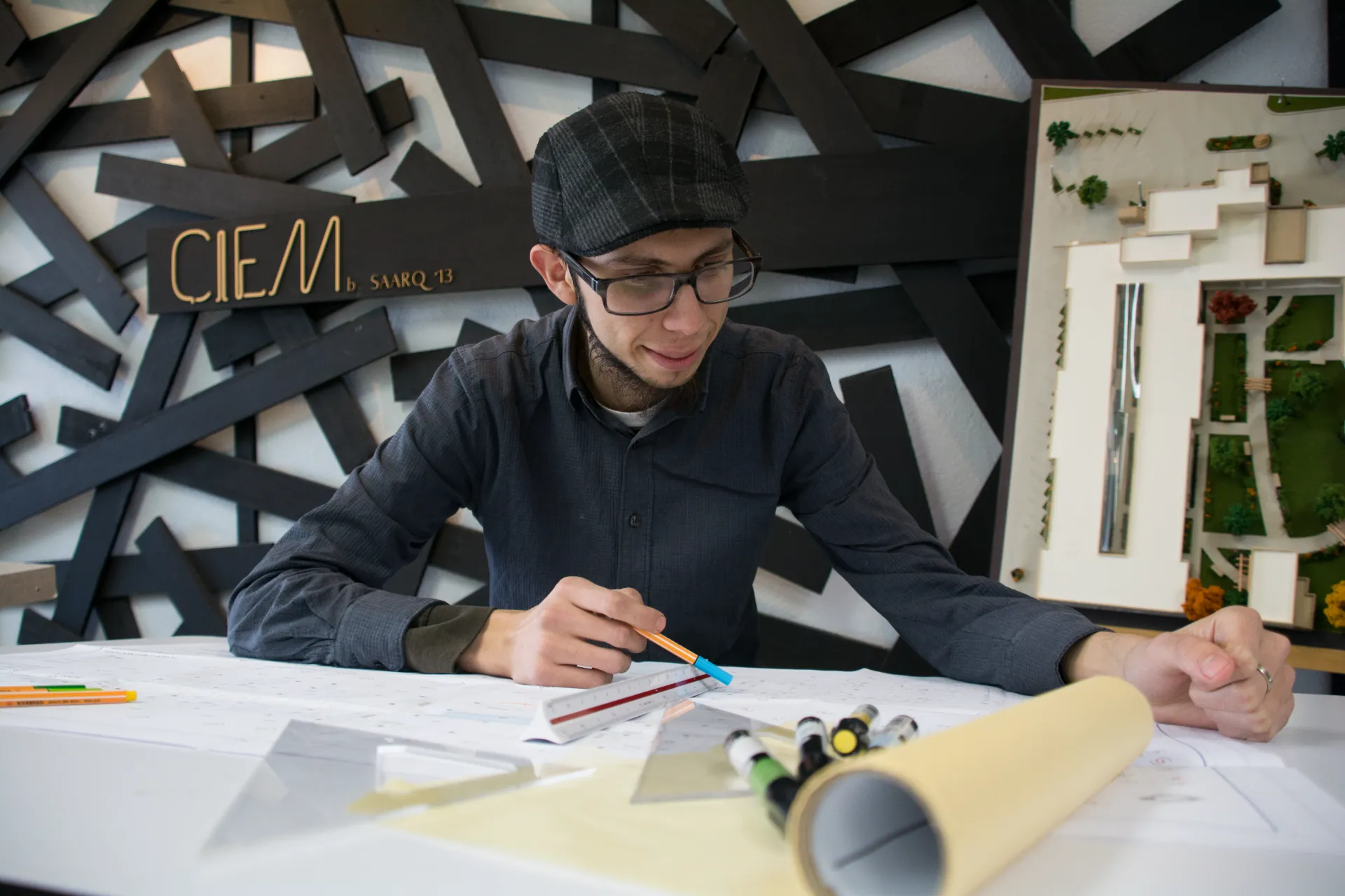 Jóven sonriente trabajando en una mesa con material de arquitectura alrededor 
