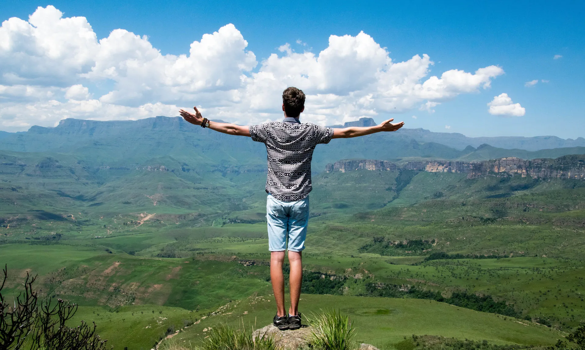 Joven de espalda en la cima con los brazos abiertos y con la mirada al horizonte
