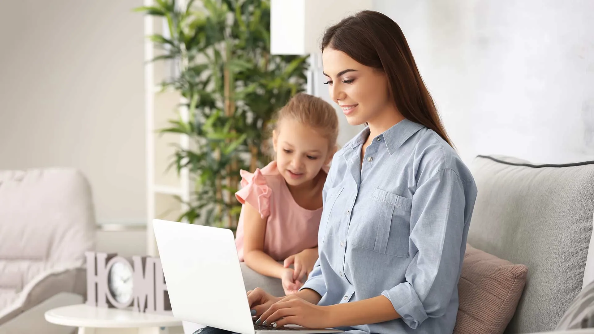 Madre de familia trabajando en su laptop, con su hija a una lado