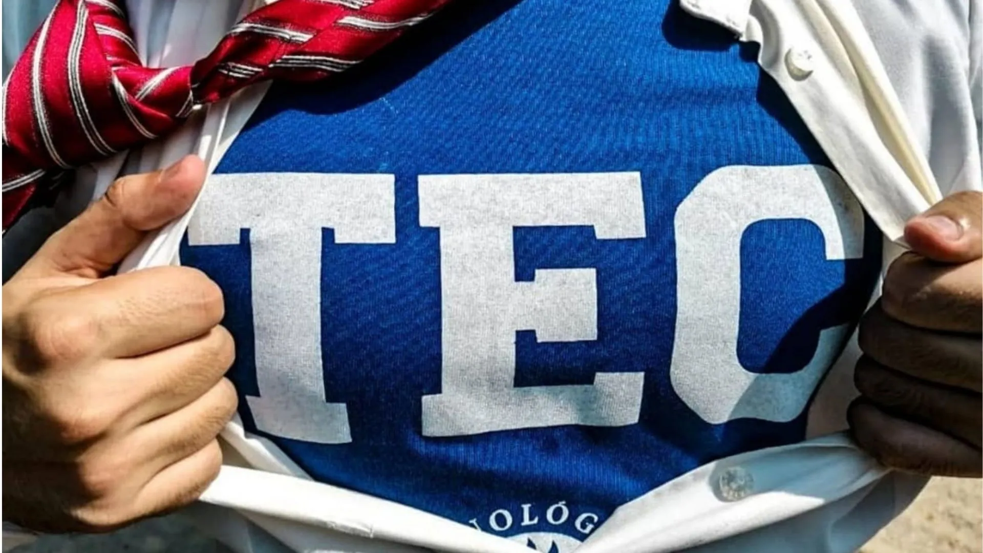 Persona que se abre la playera para poder apreciar la playera TEC de fondo.