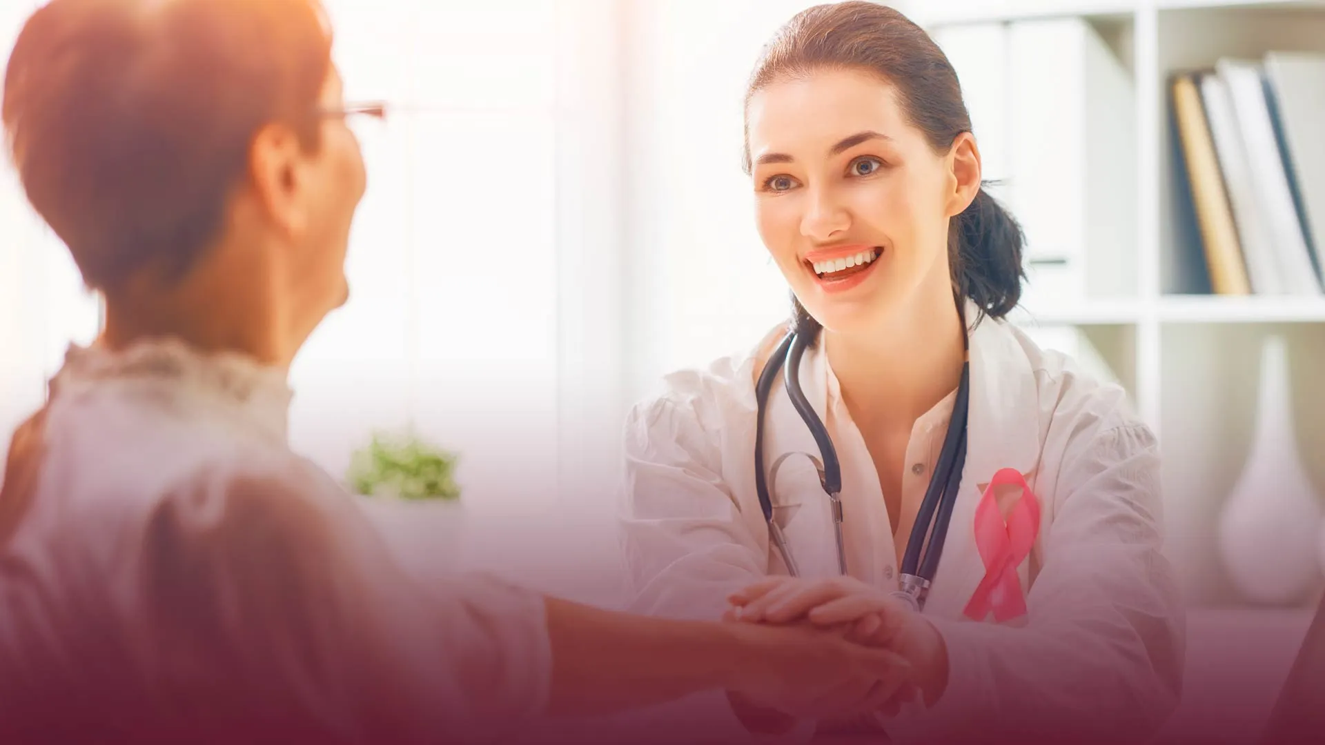 Doctora portando listón rosa y paciente, temática prevención cáncer de mama