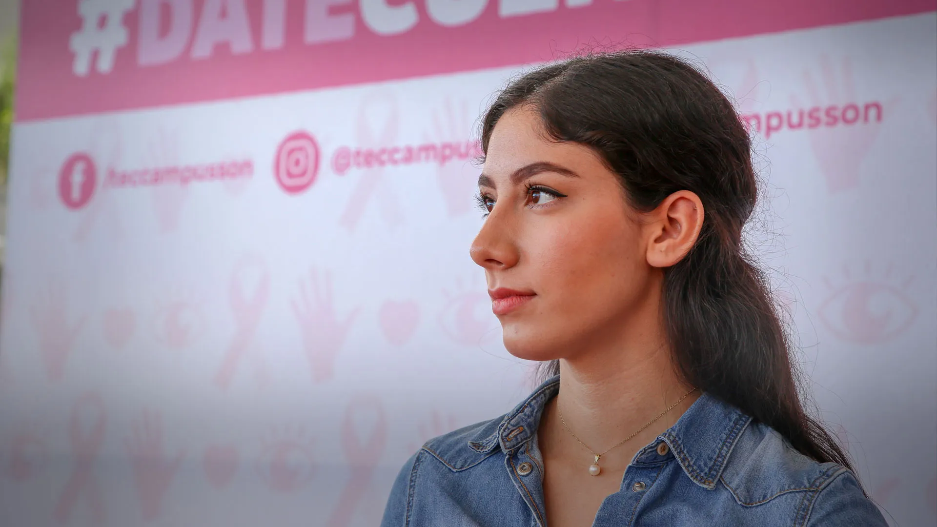 Joven mexicana, detrás de ella se encuentra un anuncio para motivar a prevenir el cáncer de mama