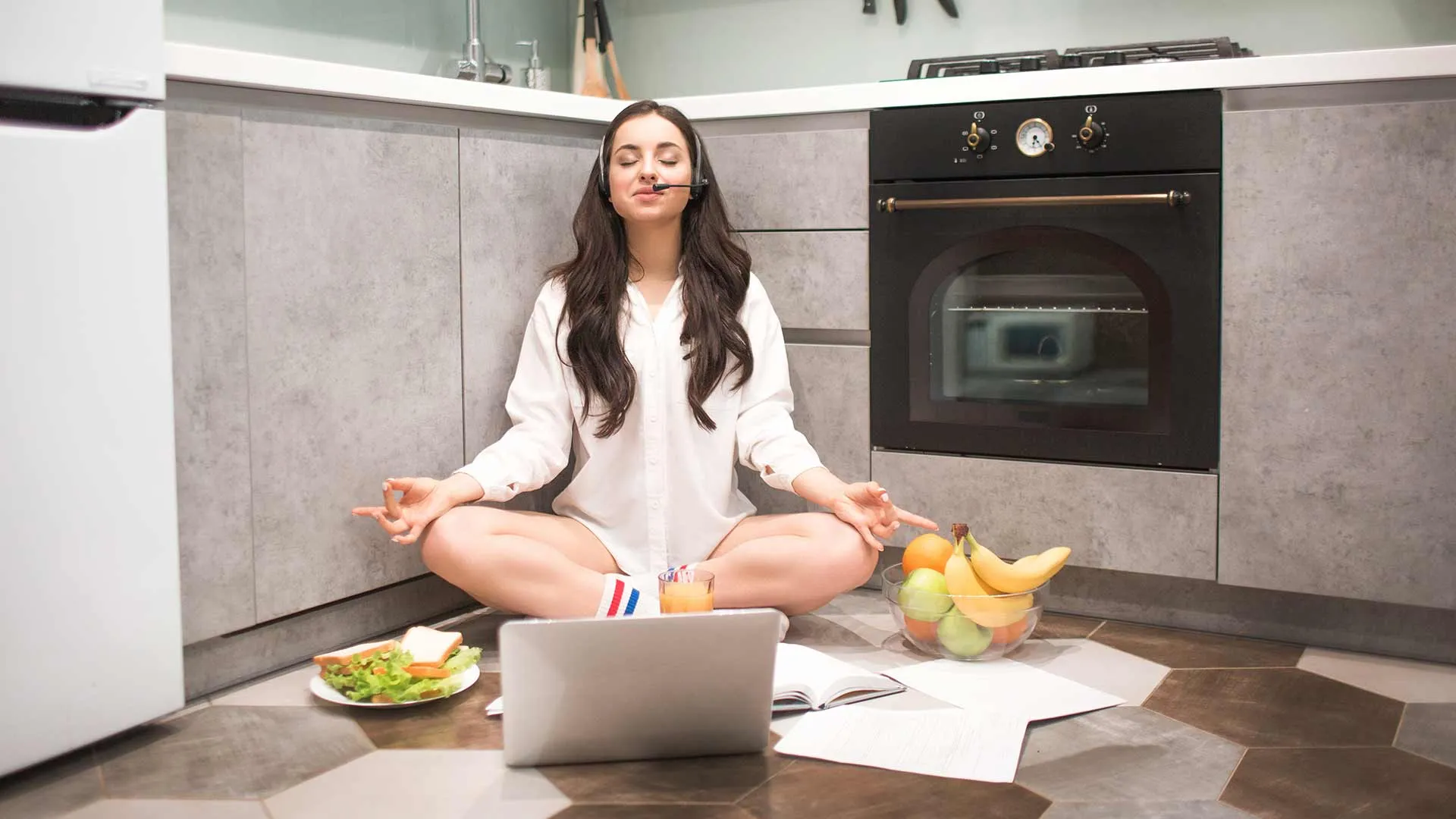 Joven con computadora, en posición de yoga y comida saludable alrededor, para representar el concepto de una rutina equilibrada