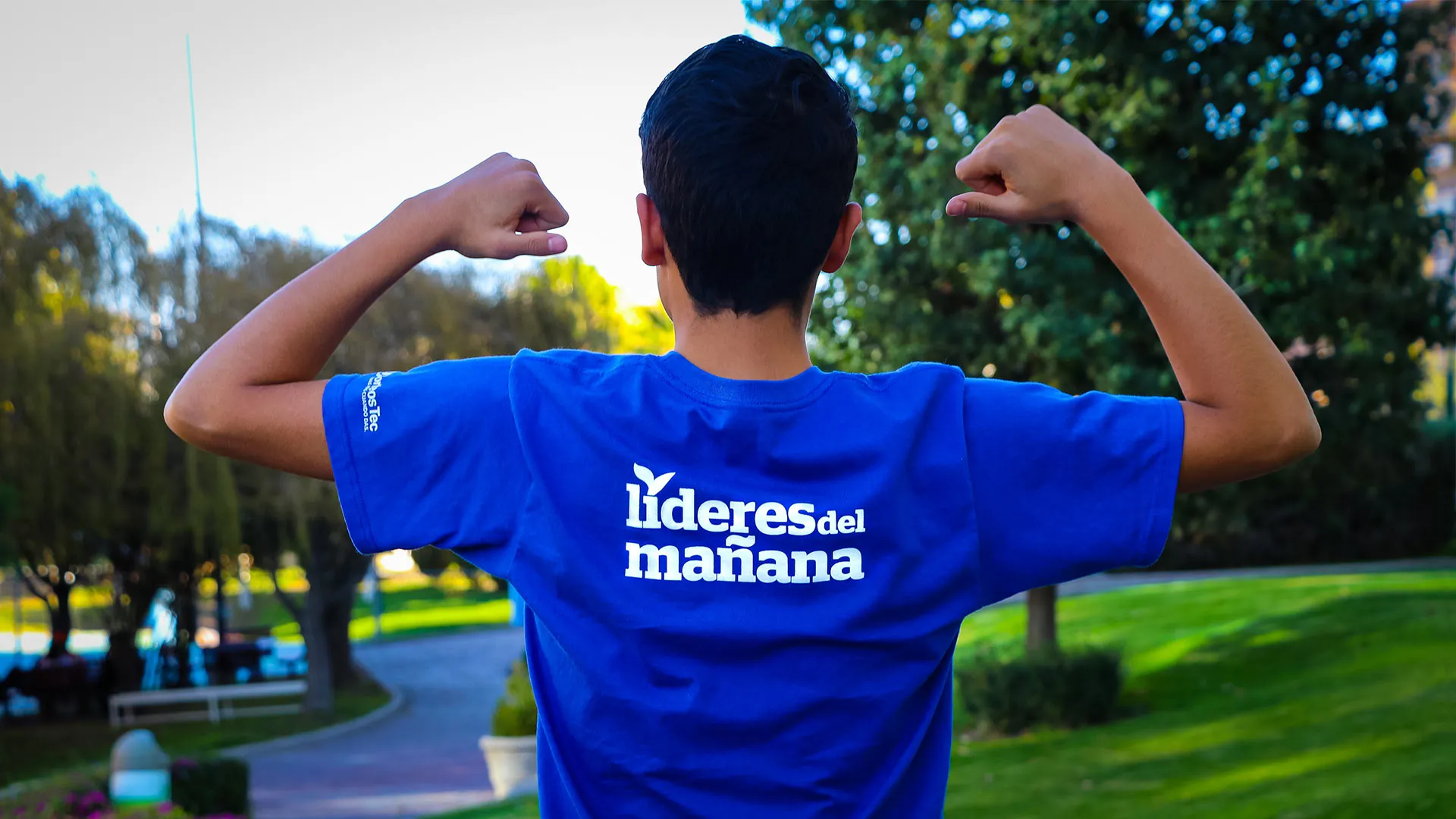 Chico de espaldas señalando la playera que dice: Líderes del Mañana