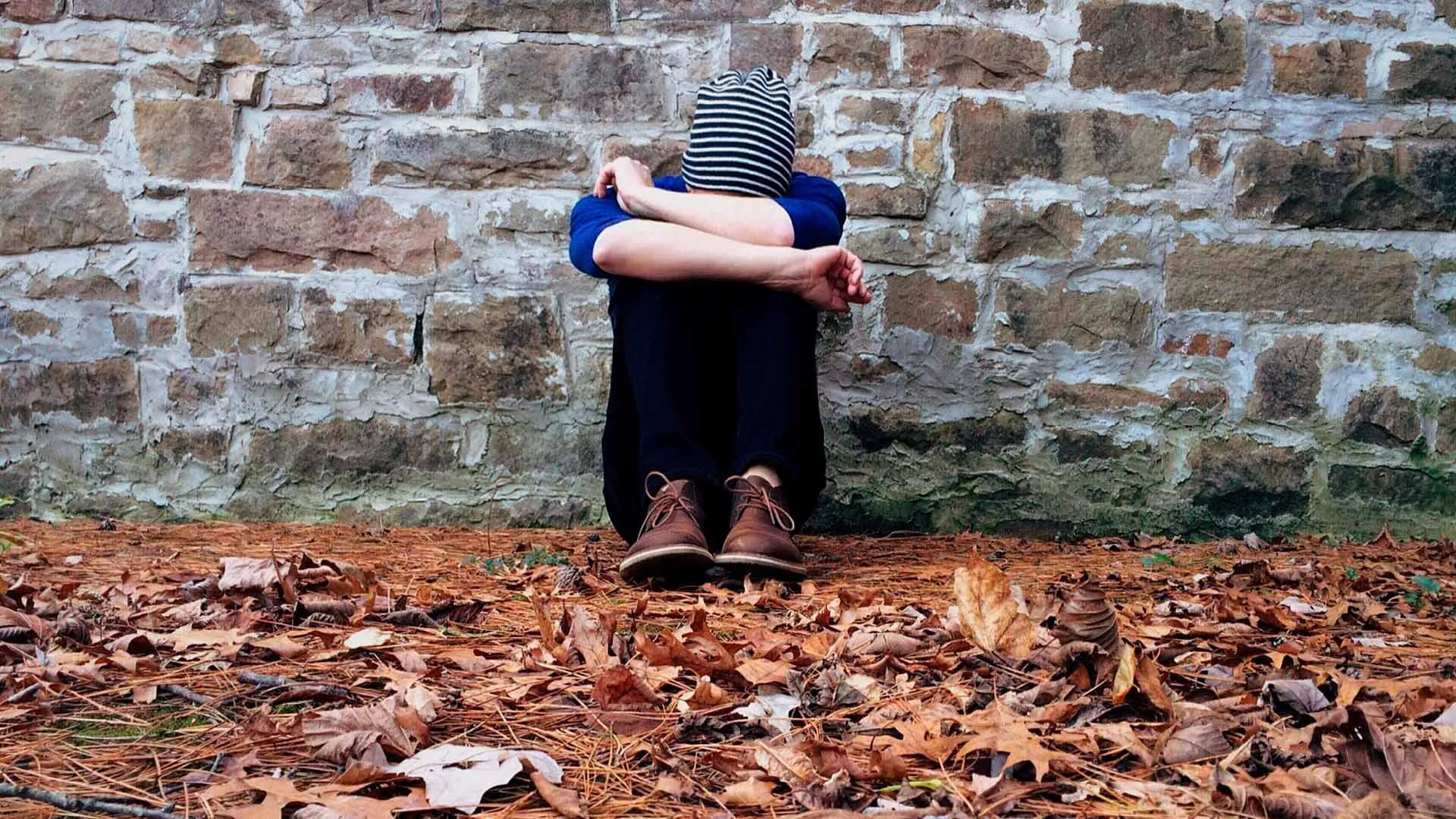 Joven sentado en el piso cubriendo su cabeza con los brazos.