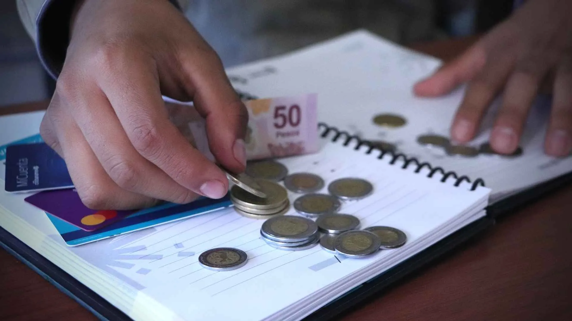 Persona cuenta dinero en escritorio con libreta y tarjetas bancarias