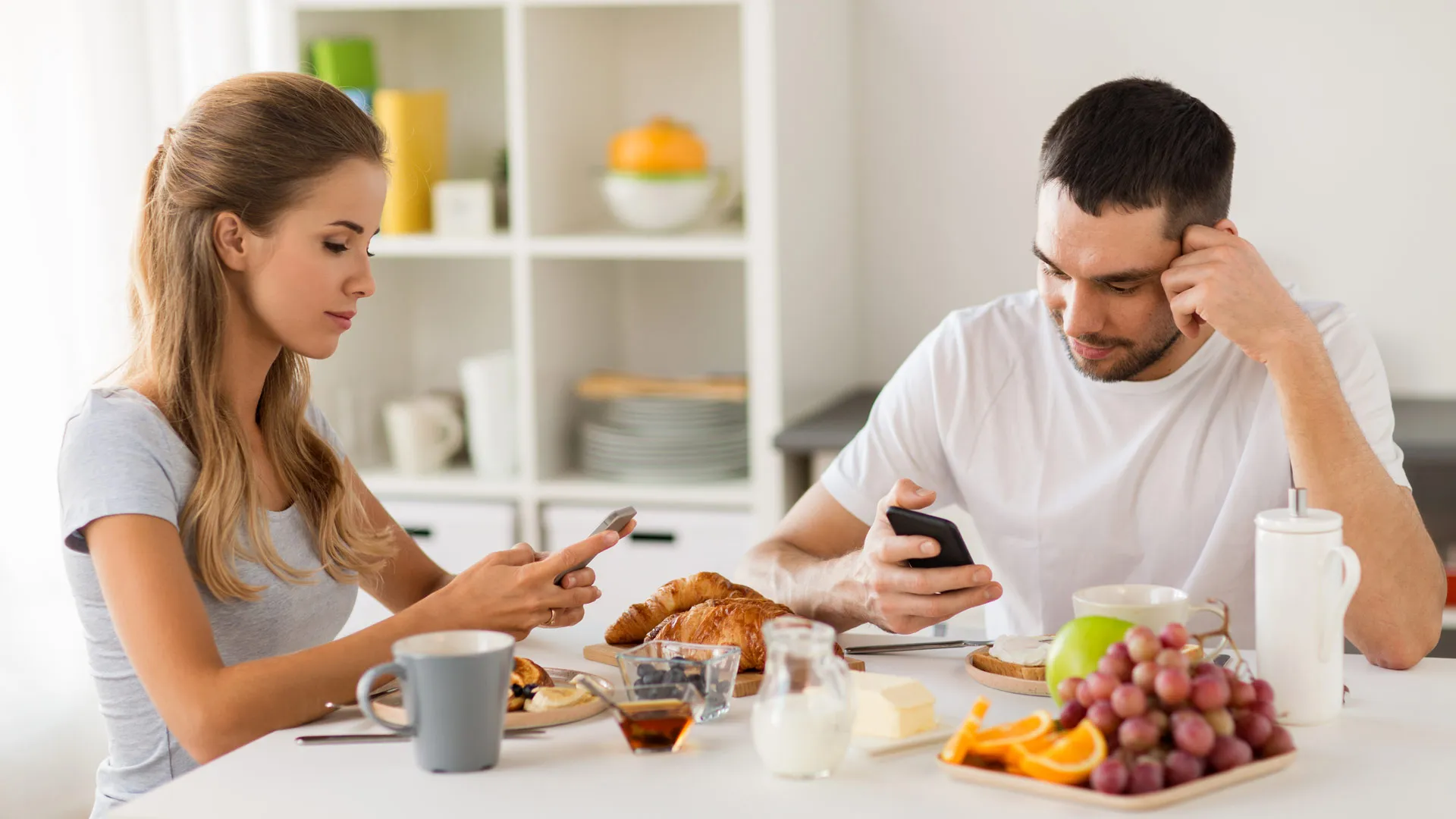 Dos personas comiendo mientras revisan sus dispositivos móviles.