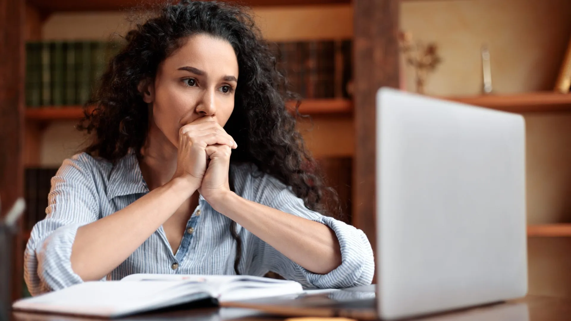 Mujer frente a laptop, con manos en la boca, signo de preocupación