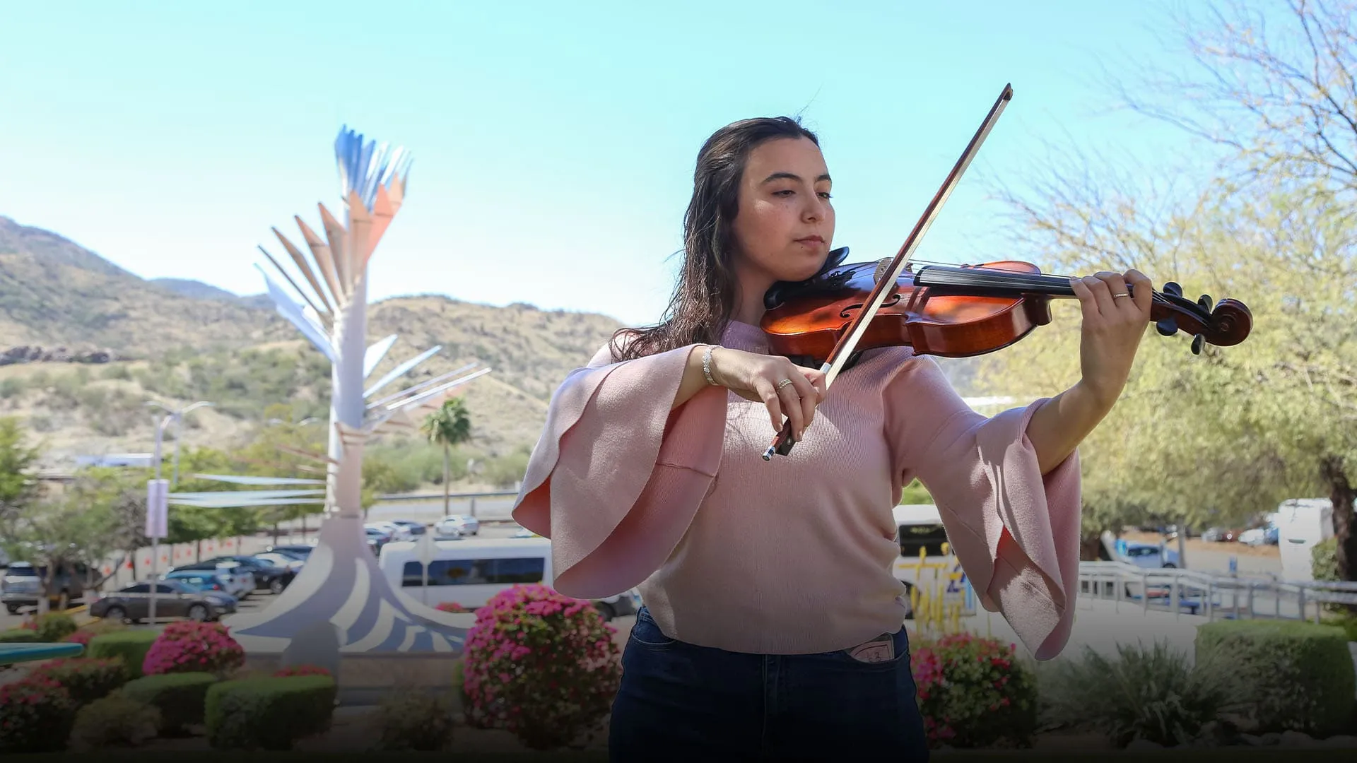 Mariana Páez tocando la viola frente a una vista de la Cápsula del Tiempo del campus Sonora Norte