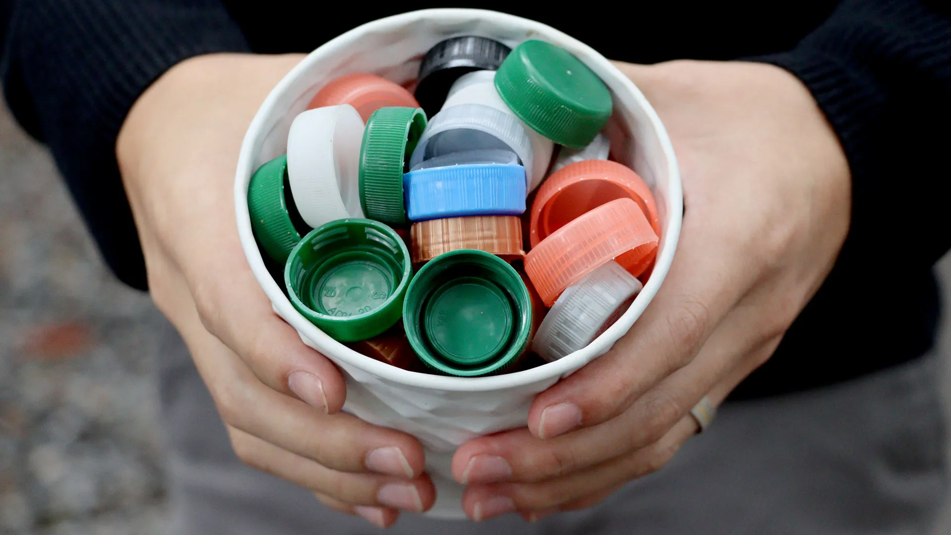 Hombre sostiene recipiente lleno de tapas de plástico.