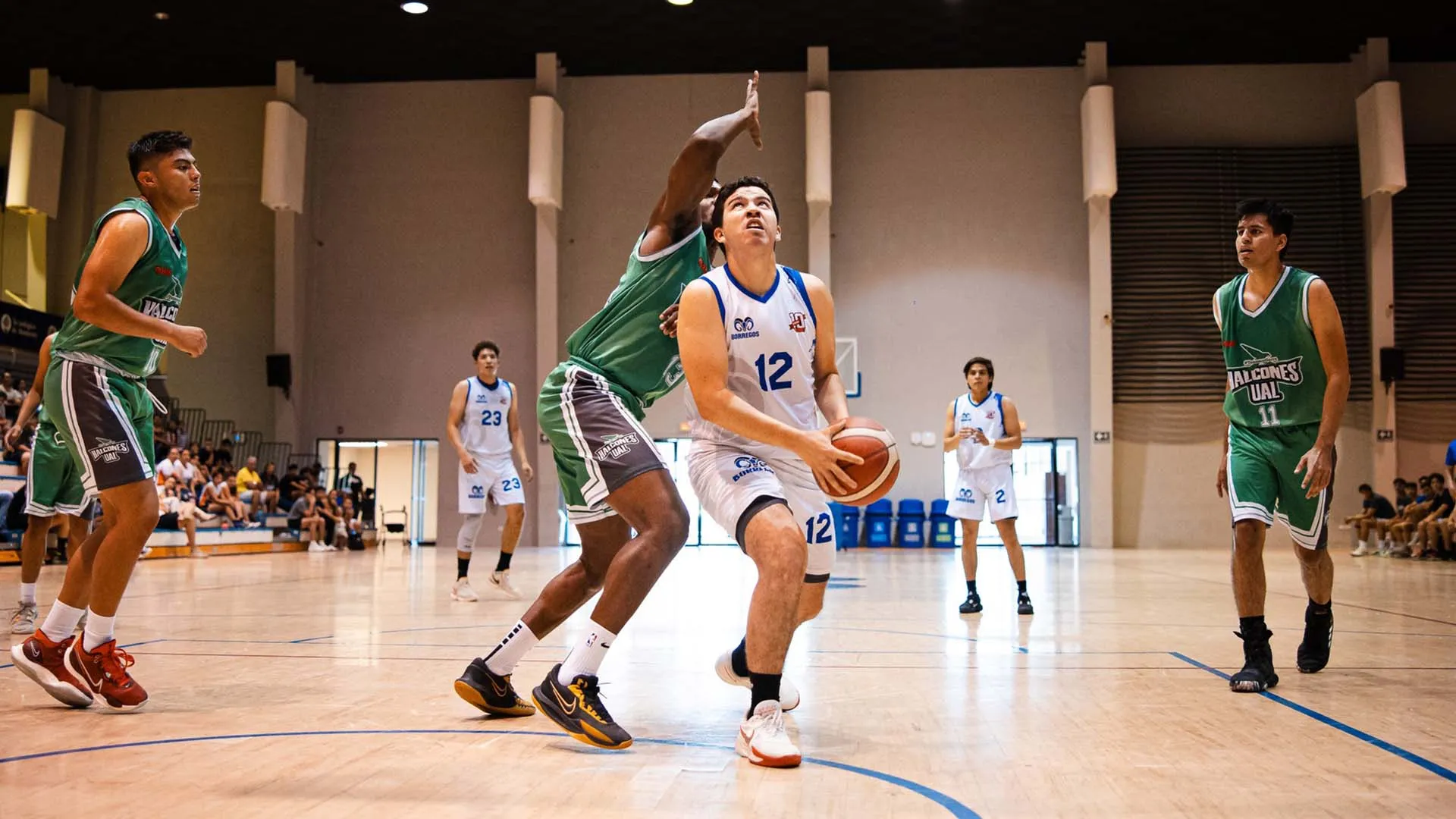 Jugador de Borregos Laguna con uniforme blanco disputa un enceste de básquetbol contra un atleta que viste jersey verde
