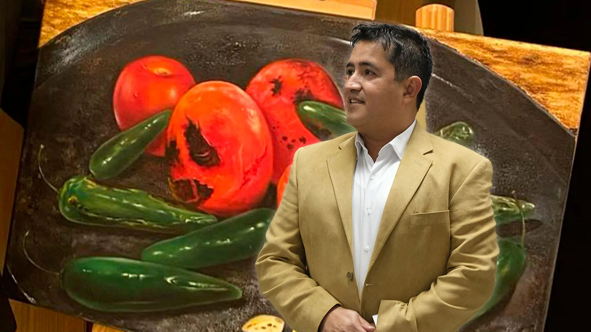 Profesor de arte usa traje color café y de fondo tiene una de sus pinturas en óleo con tomates y chiles