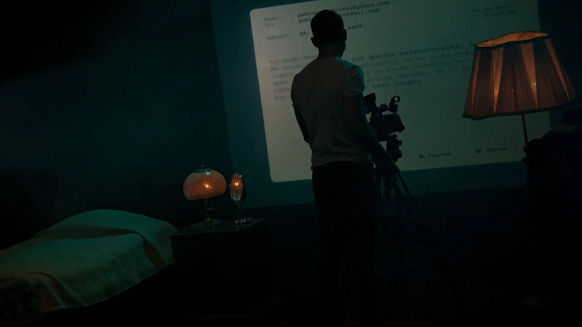 Vista de espalda del profesor Gonzalo Murúa sosteniendo una cámara de vídeo sobre un tripié, frente a una proyección de un cuento de su padre. 