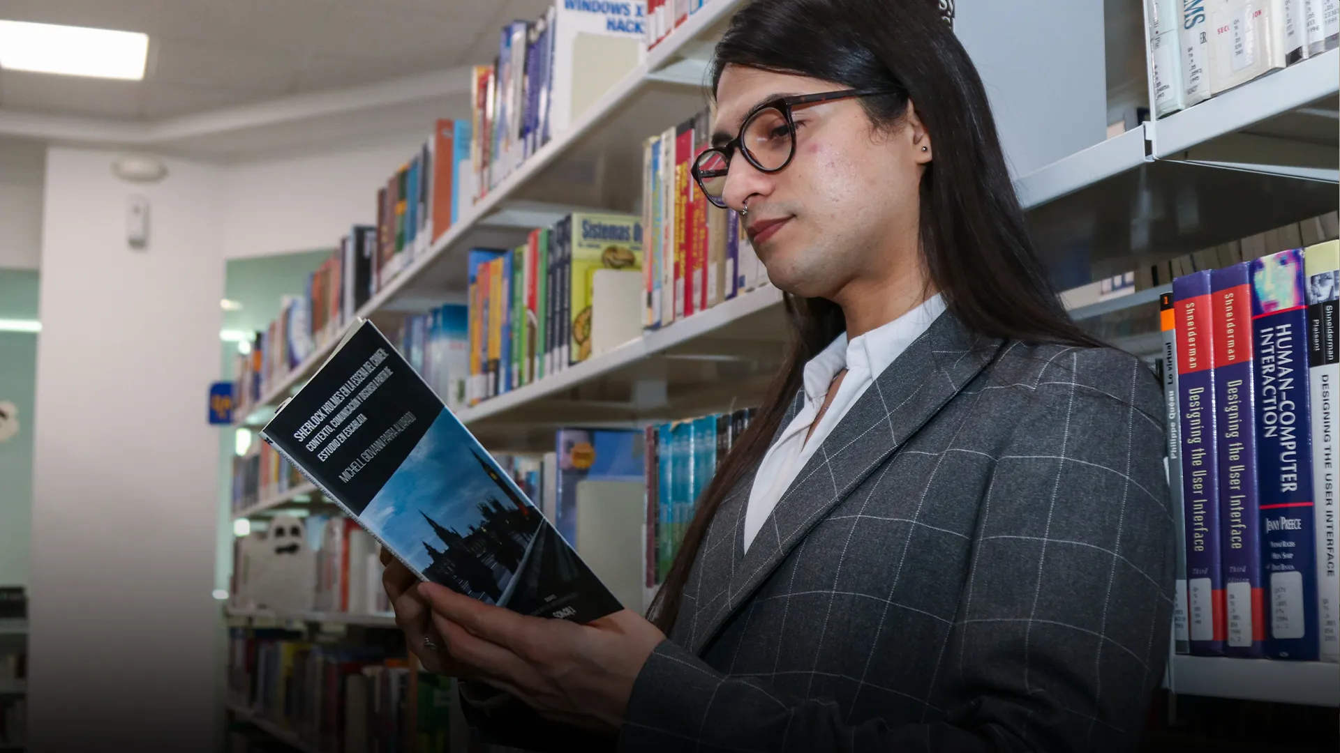 Profesor leyendo libro recargado contra un librero