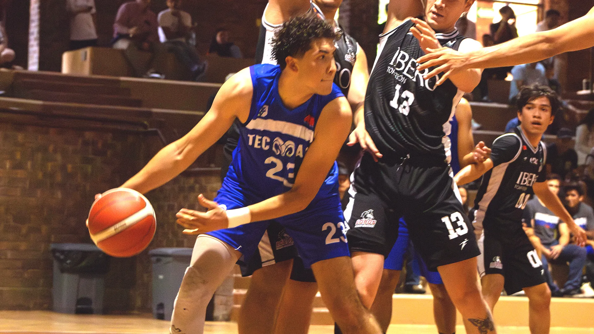 Jugador de básquetbol con uniforme de Borregos Laguna disputa el juego contra atletas con uniforme negro