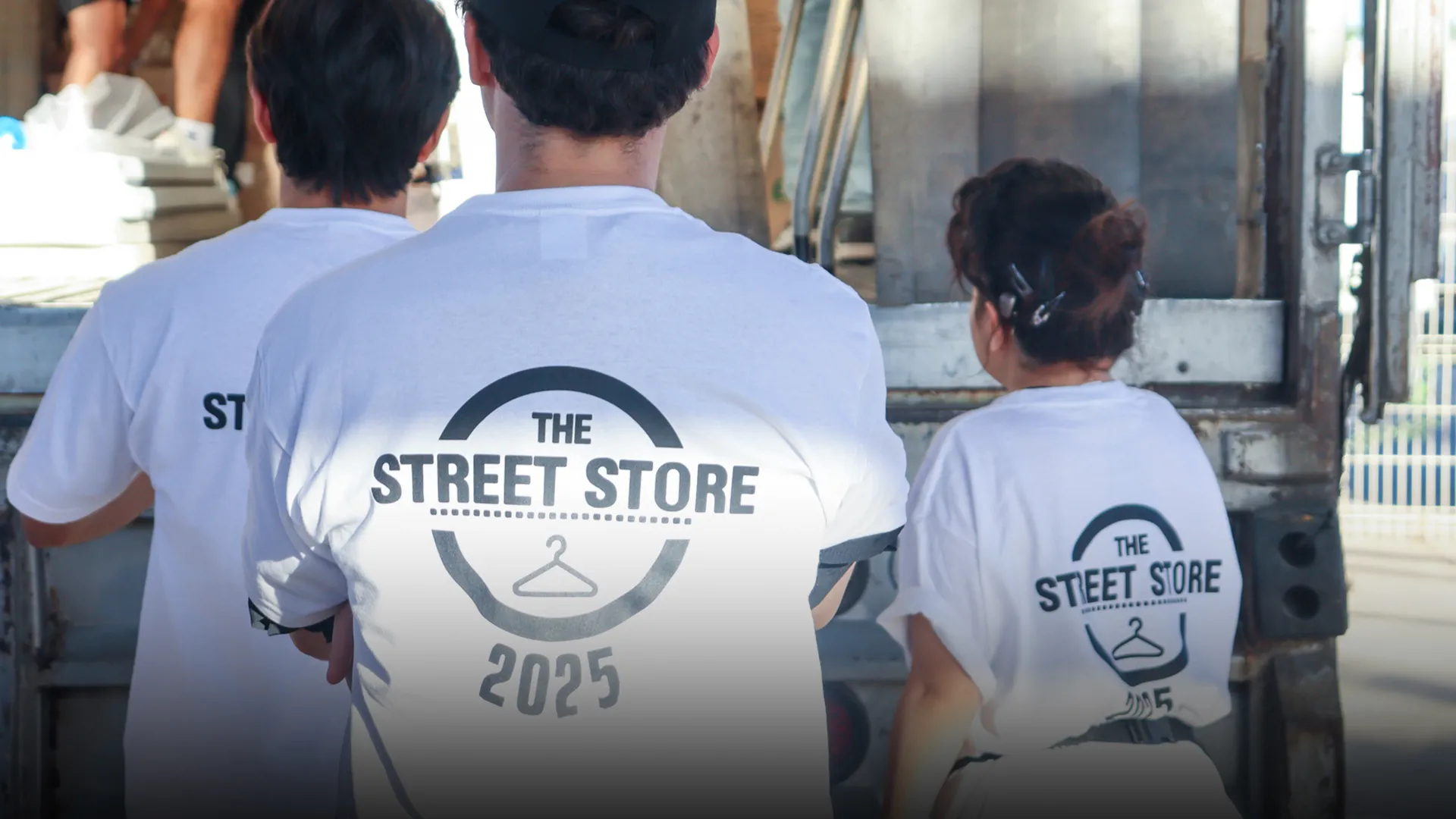 Vista de espaldas de tres voluntarios portando camisetas blancas con un logo que dice Street Store 2025