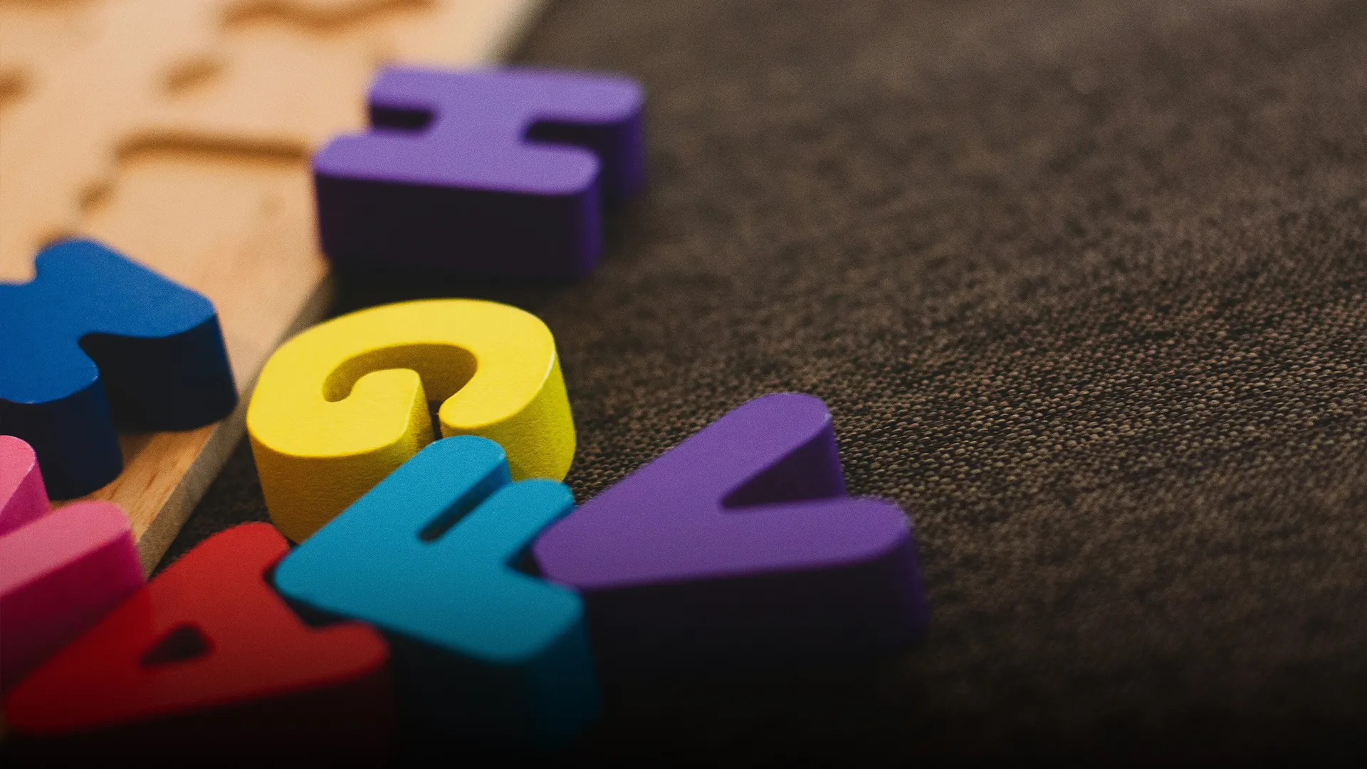 Letras coloridas de madera sobre alfombra oscura.