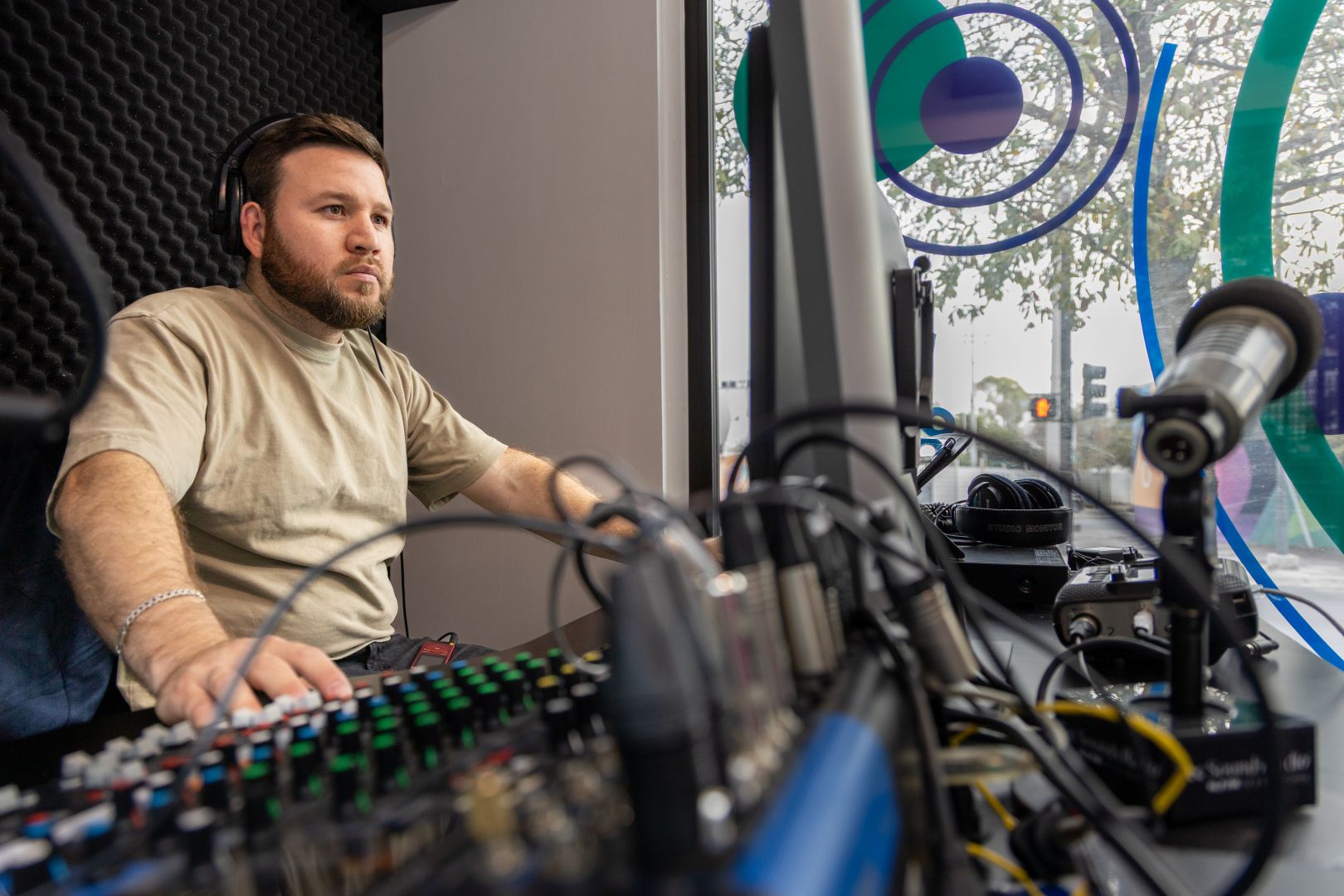 Operador de audio con aud&iacute;fonos manipula la consola durante una transmisi&oacute;n en cabina de radio.
