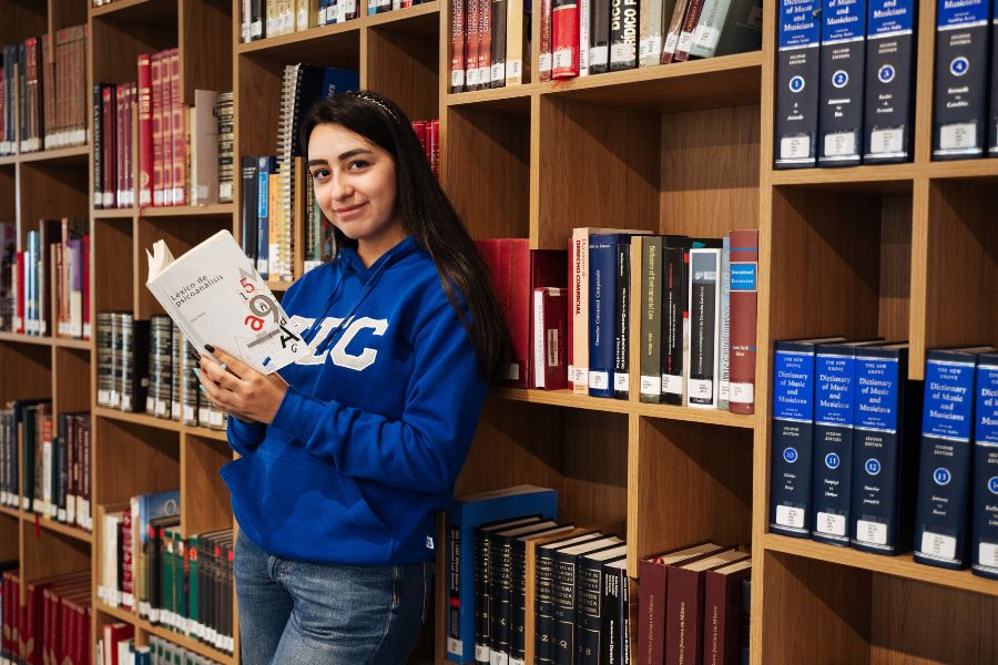 Estudiante de Medicina sostiene un libro en una biblioteca rodeada de estanter&iacute;as con textos especializados en ciencias de la salud.