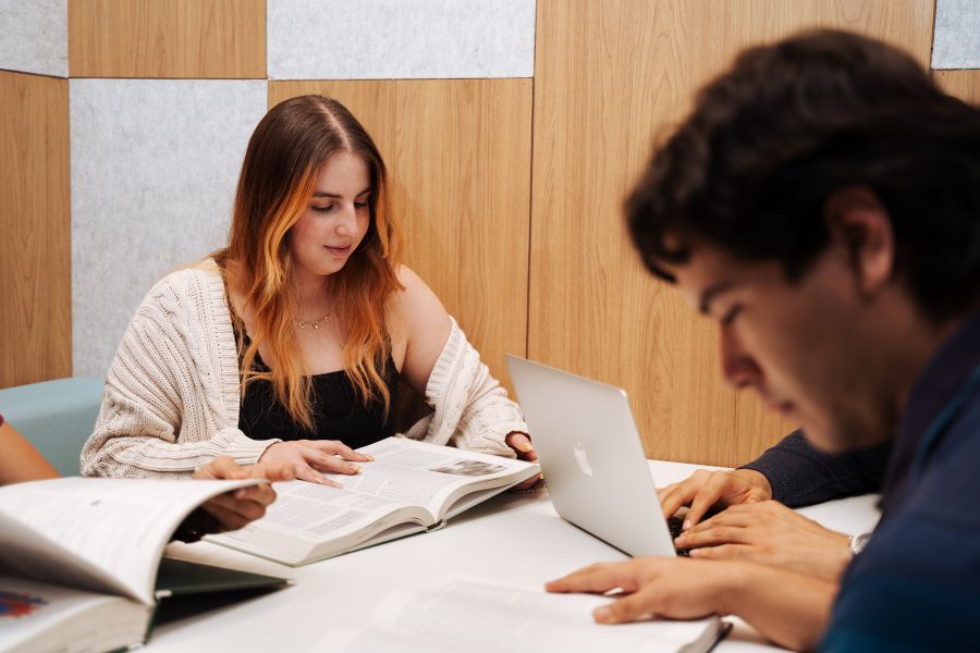 Dos estudiantes revisan material acad&eacute;mico y trabajan con una computadora port&aacute;til en una sala de estudio dentro de las instalaciones de la Escuela de Medicina.