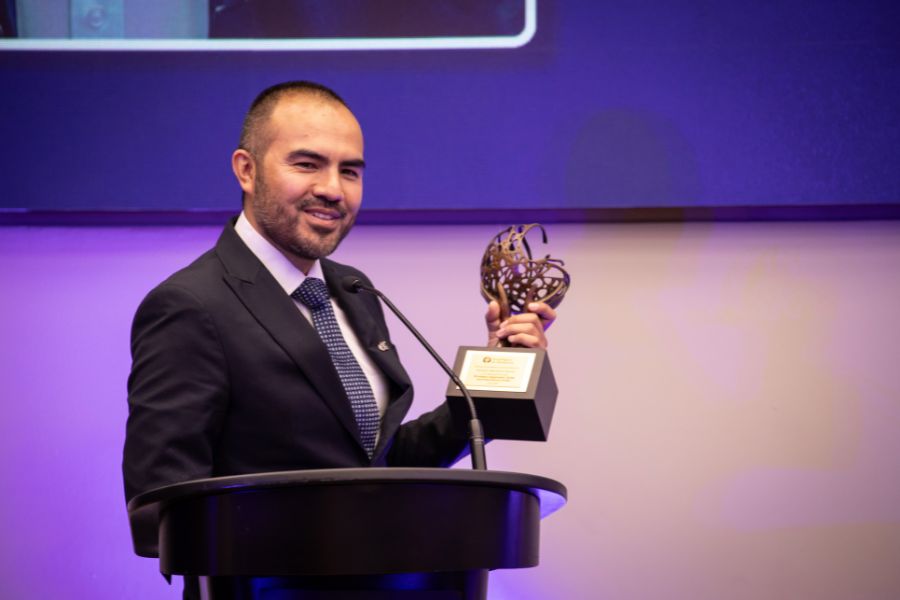 Rodolfo Mendoza G&oacute;mez sostiene el reconocimiento mientras ofrece un mensaje desde el podio durante la ceremonia del Premio Profesor Inspirador 2026.