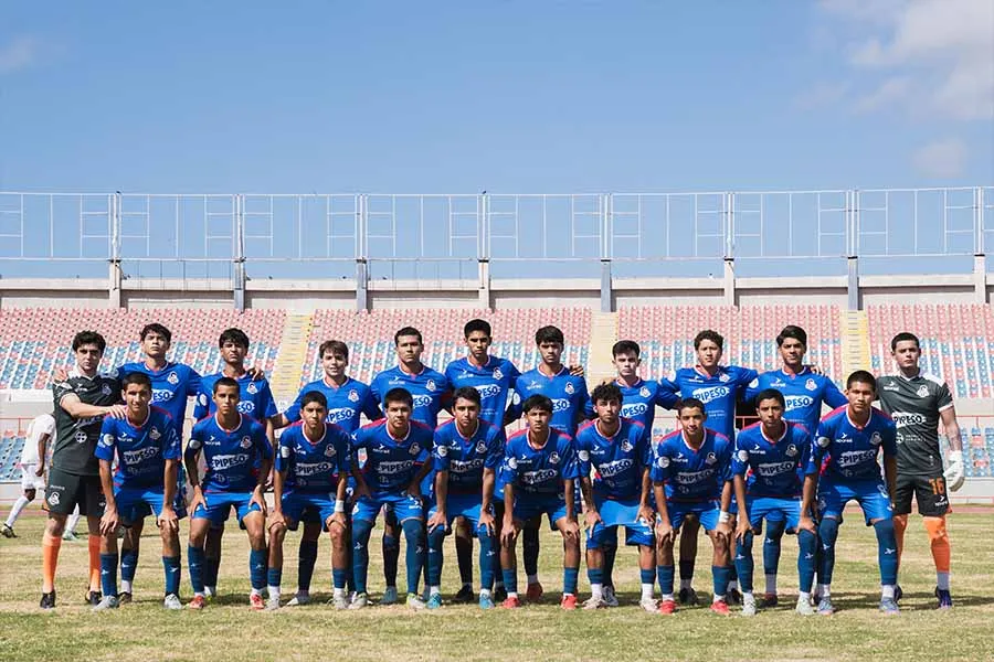 Equipo de f&uacute;tbol posando juntos en la cancha, portando uniformes azules. 