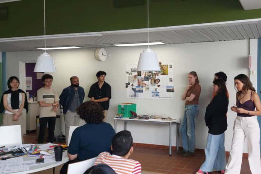 Grupo de 8 arquitectos presentando un proyecto frente a un sal&oacute;nd de clases.