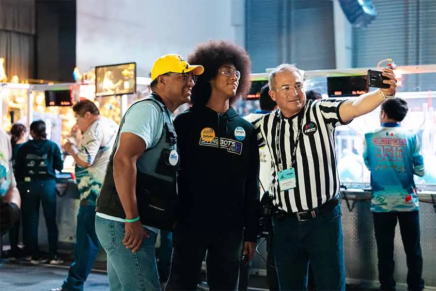 Un miembro del equipo StingBots 6702 de PrepaTec Santa Anita posa para una foto con un voluntario y un &aacute;rbitro de FIRST Robotics Competition durante el regional en M&eacute;xico.