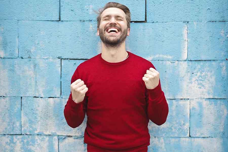humbre con sudadera roja, con las manos al nivel del pecho, puños cerrados y sonriendo