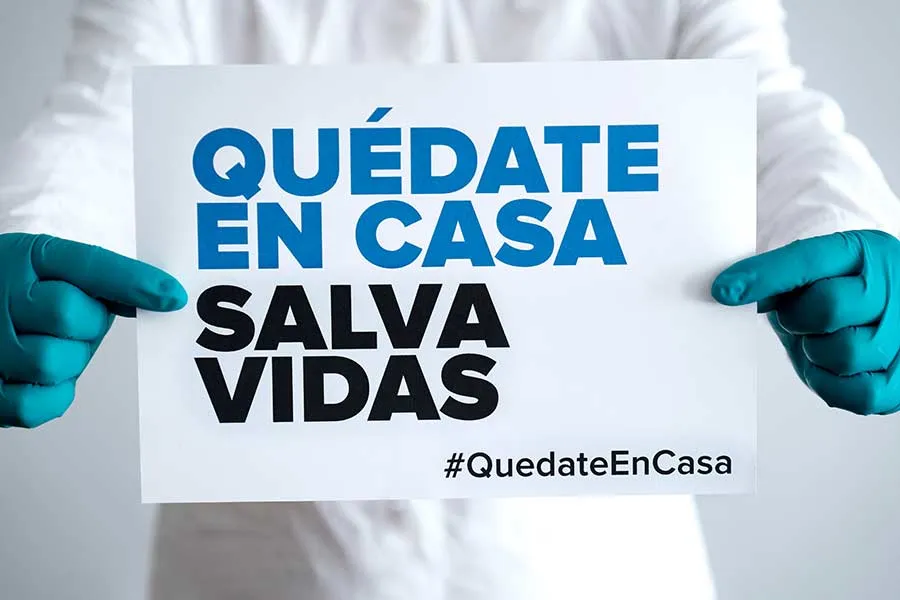 Persona sosteniendo en sus manos un letrero con el mensaje "Qu&eacute;date en casa, salva vidas"