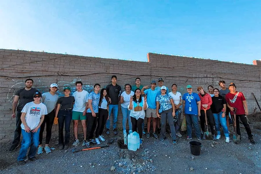 Cartel o señalización del proyecto PlantOn con árboles recién plantados y estudiantes al fondo, en preparación para la edición 2025.