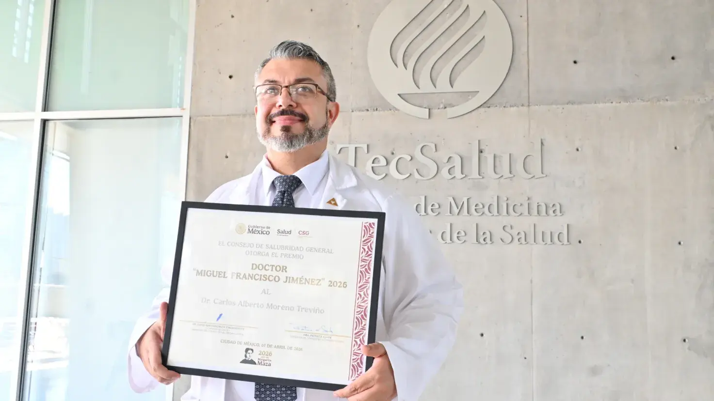 Doctor Carlos Moreno posando con su Premio Dr. Miguel Francisco Jiménez 2026 frente a la EMIS del Tec