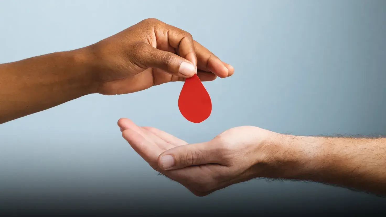 Mano sosteniendo una gota de sangre hecha de papel sobre otra mano en posición para recibirla.