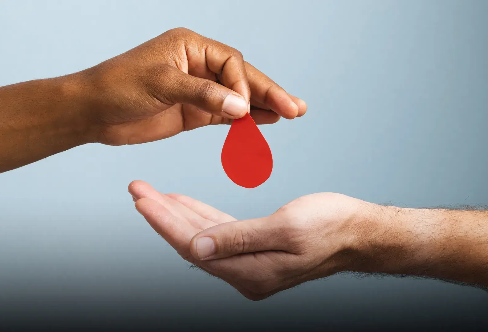 Mano sosteniendo una gota de sangre hecha de papel sobre otra mano en posición para recibirla.