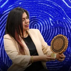 Mujer con saco blanco sosteniendo trofeo con forma de corte transversal de tronco y mirando hacia el.