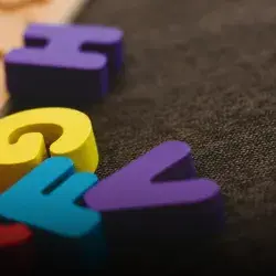 Letras coloridas de madera sobre alfombra oscura.