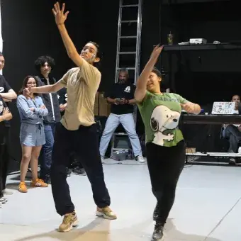 Dos jóvenes actuando en medio de un grupo de actores. 