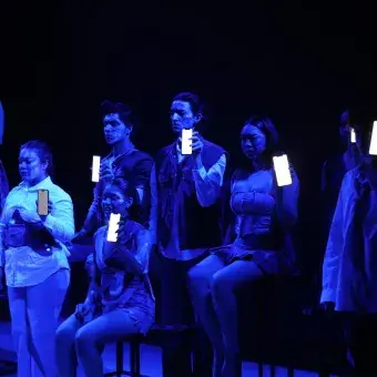 Grupo de actores sosteniendo celulares en la oscuridad. 