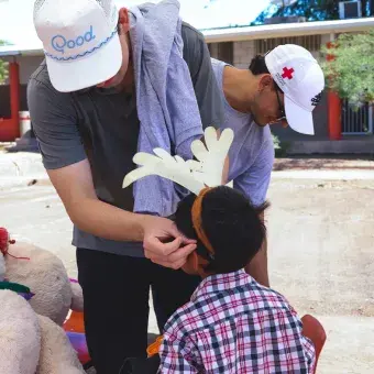 Foto: Helena Armenta Joven voluntario acomodando diadema con decoración en cabeza de niño.