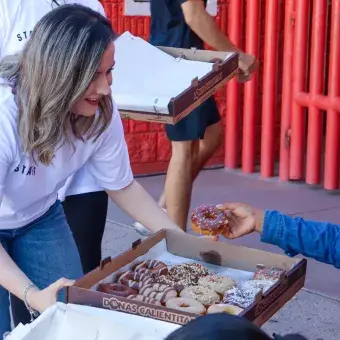 Foto: Emilio Morales Mujer repartiendo donas a personas sentadas en sillas.
