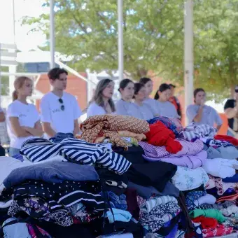 Se recaudaron más de 3 toneladas de ropa para ser donadas. Foto: Helena Armenta Mesas con ropa doblada y apilada con personas formadas en el fondo.