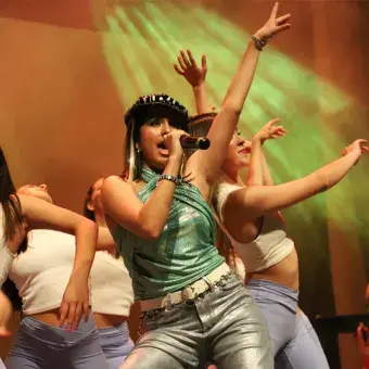 Foto: Diego Beltrán Chica con blusa brillante verde y boina canta rodeada de bailarinas vestidas de blanco.