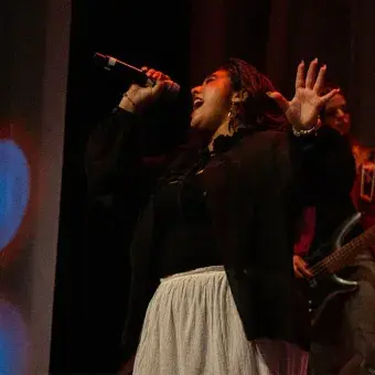 Foto: Blas Murillo Chica cantando en escenario con top negro y falda blanca.