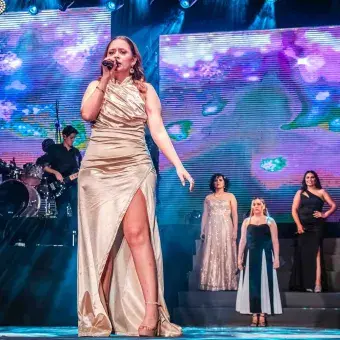 Cantante con vestido largo color dorado interpreta canción como solista en ensamble musical del 50 aniversario