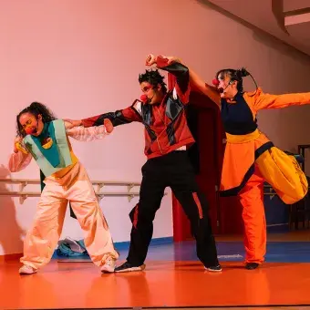 Tres actores con vestuarios y narices de payaso fingiendo pelear.