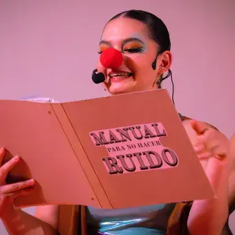 Actriz con vestuario y nariz de payaso  sosteniendo un folder en sus manos mientras lee. 