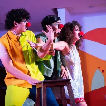 Tres actores con vestuarios y narices de payaso viendo hacia la derecha.